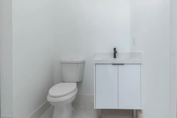 Bathroom featuring toilet, marble finish floor, baseboards, and vanity