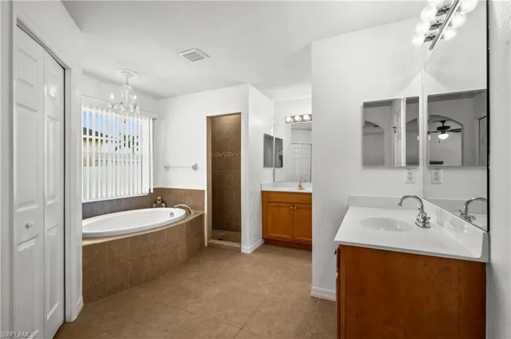 Full bathroom with two vanities, a garden tub, a shower stall, light tile patterned flooring, and a closet