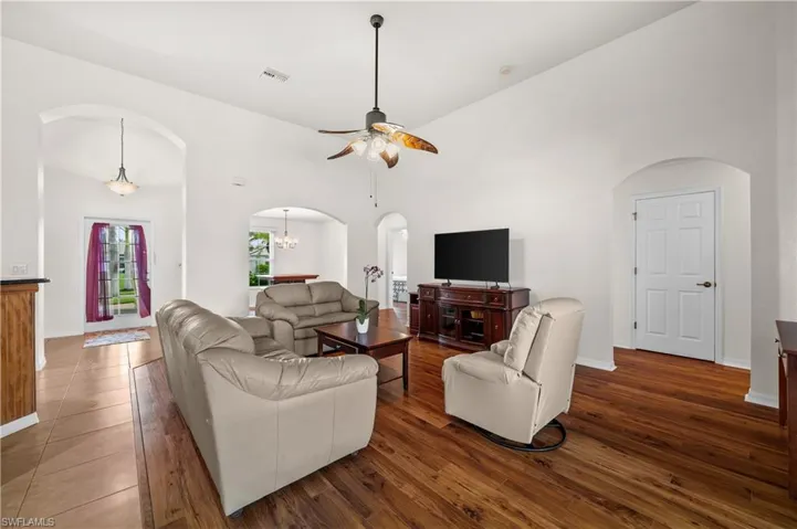 Living room featuring arched walkways, high vaulted ceiling, ceiling fan, dark wood-style floors, and a chandelier