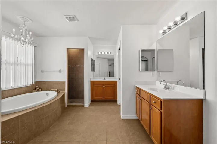 Full bathroom featuring two vanities, a bath, light tile patterned flooring, a stall shower, and a chandelier