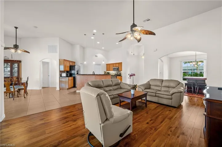 Living area featuring arched walkways, a ceiling fan, a high ceiling, a chandelier, and light wood-style floors