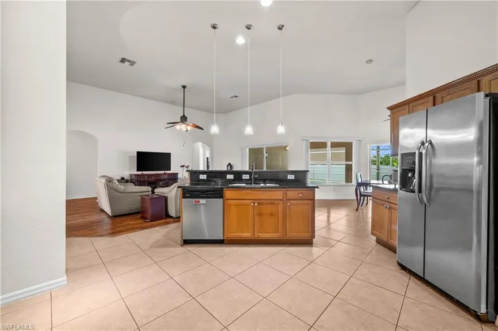 Kitchen featuring appliances with stainless steel finishes, brown cabinets, open floor plan, light tile patterned flooring, and pendant lighting