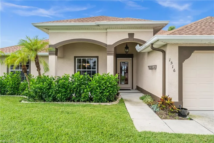 Doorway to property featuring an attached garage, stucco siding, a lawn, and a shingled roof