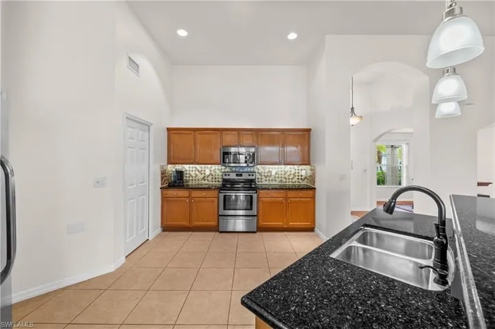 Kitchen with tasteful backsplash, light tile patterned flooring, pendant lighting, appliances with stainless steel finishes, and a high ceiling