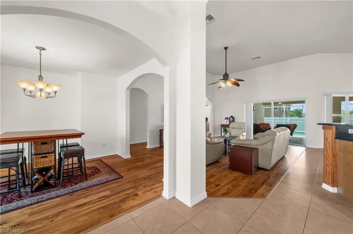Tiled living room featuring lofted ceiling, arched walkways, a chandelier, and ceiling fan