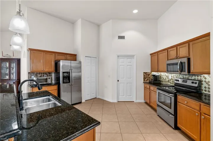 Kitchen with tasteful backsplash, stainless steel appliances, brown cabinets, a towering ceiling, and light tile patterned floors