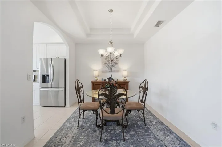 Dining space featuring arched walkways, a tray ceiling, light tile patterned floors, and a chandelier