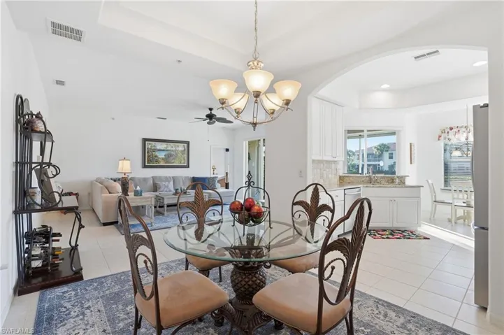 Dining room with a tray ceiling, light tile patterned floors, a ceiling fan, a chandelier, and recessed lighting