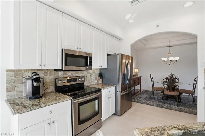 Kitchen with stainless steel appliances, light stone countertops, white cabinets, hanging light fixtures, and backsplash