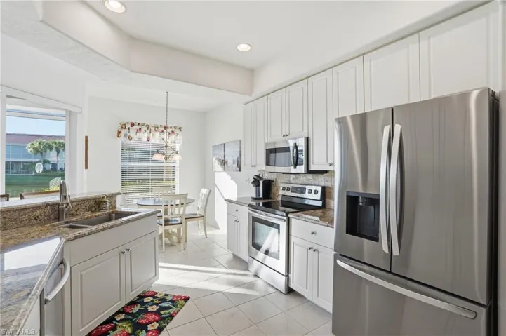 Kitchen with stainless steel appliances, white cabinetry, backsplash, light stone countertops, and recessed lighting