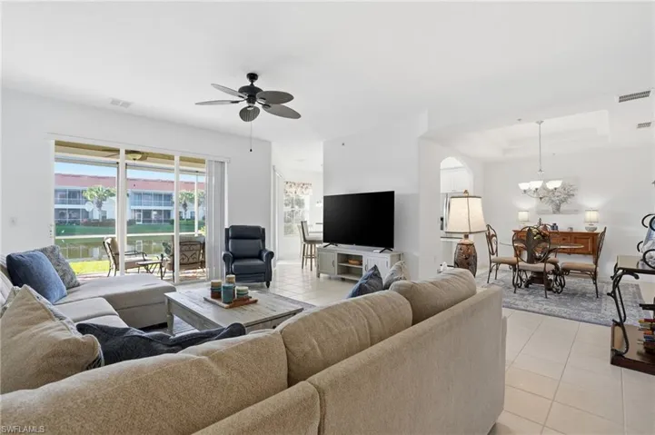 Living room with light tile patterned floors, a tray ceiling, ceiling fan, and a chandelier