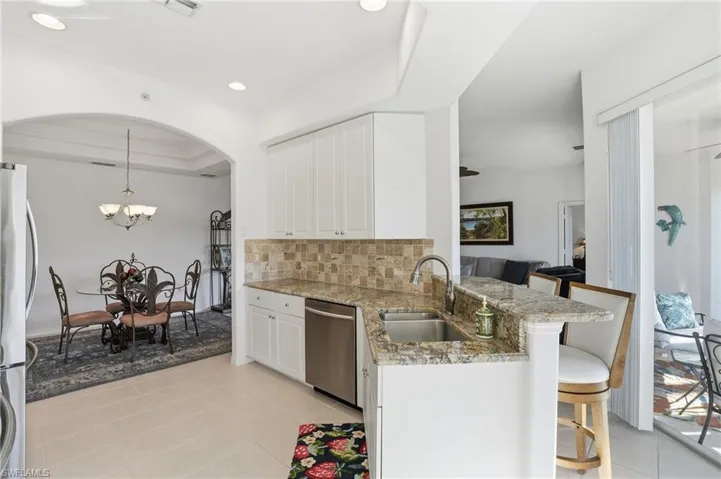 Kitchen with light stone countertops, white cabinetry, appliances with stainless steel finishes, backsplash, and arched walkways