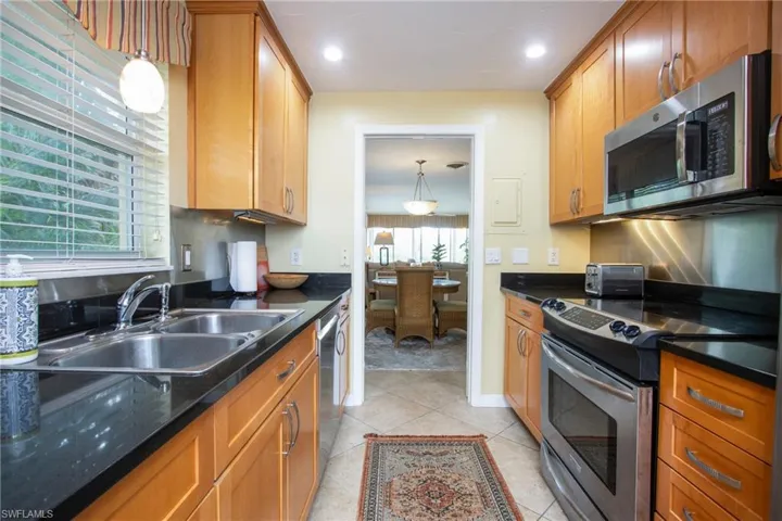 Kitchen with stainless steel appliances, dark stone counters, sink, decorative light fixtures, and light tile patterned floors