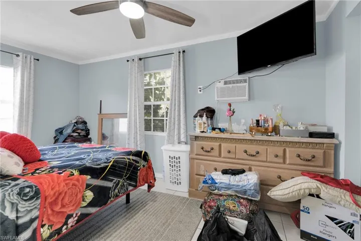 Bedroom with light tile patterned flooring, ceiling fan, a wall mounted air conditioner, and crown molding