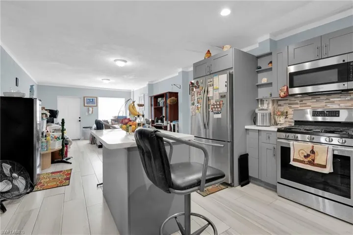 Kitchen with ornamental molding, stainless steel appliances, light countertops, gray cabinets, and open shelves