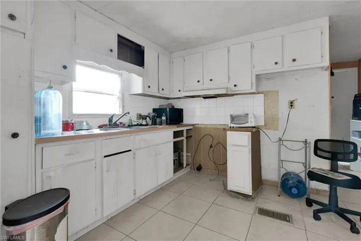 Kitchen featuring white cabinetry, black microwave, light countertops, and decorative backsplash