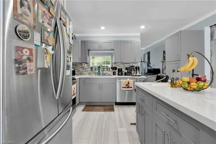 Kitchen with gray cabinets, stainless steel appliances, light stone counters, crown molding, and decorative backsplash