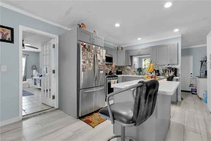 Kitchen with gray cabinets, appliances with stainless steel finishes, crown molding, backsplash, and a breakfast bar