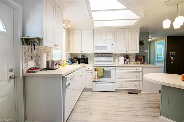 Kitchen with white appliances, light wood-style flooring, decorative backsplash, a sink, and light countertops