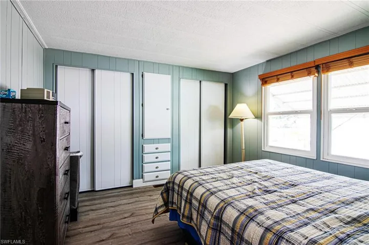 Bedroom featuring dark wood finished floors, multiple closets, a textured ceiling, and wood walls