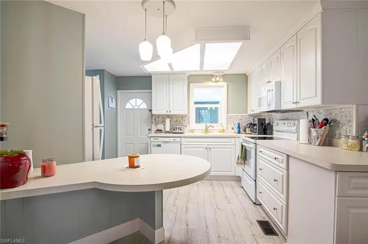Kitchen with white appliances, decorative backsplash, light wood-style floors, and light countertops