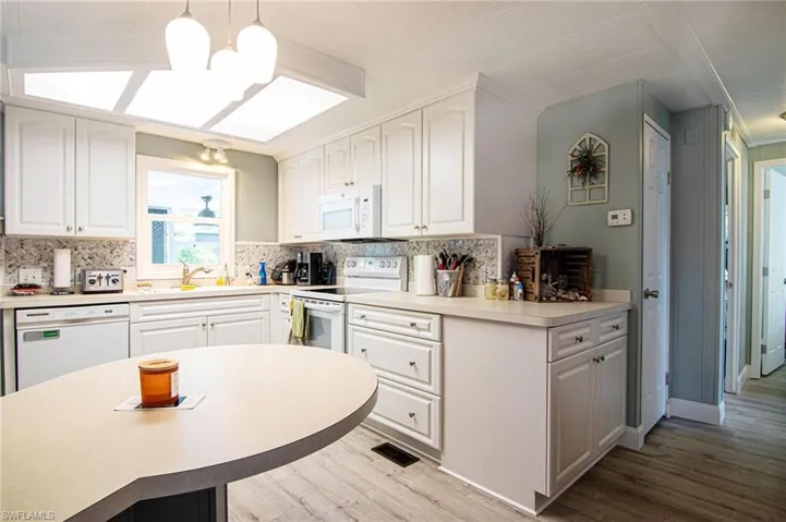 Kitchen with white appliances, wood finished floors, and backsplash