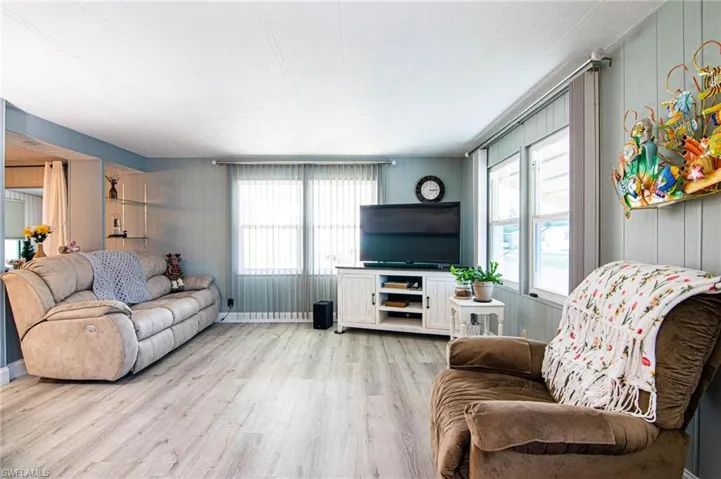 Living room with light wood-type flooring, plenty of natural light, a decorative wall, and wood walls
