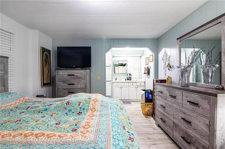 Bedroom featuring light wood finished floors, arched walkways, and connected bathroom