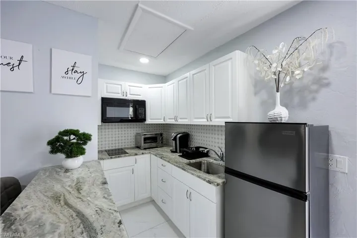 Kitchen featuring black appliances, light stone counters, white cabinets, light marble finish floors, and backsplash