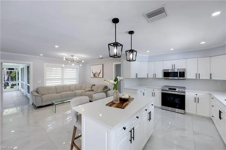 Kitchen featuring stainless steel appliances, open floor plan, ornamental molding, a kitchen bar, and white cabinetry