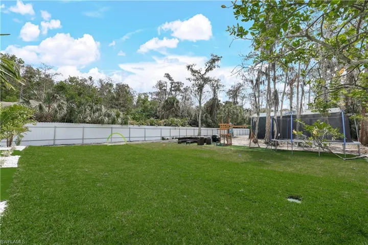 Fenced backyard with a trampoline, a patio area, and a playground