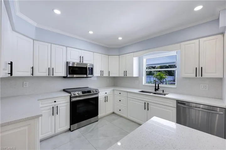 Kitchen featuring white cabinets, stainless steel appliances, crown molding, light stone counters, and recessed lighting