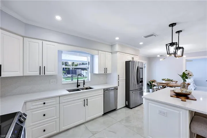 Kitchen with white cabinets, stainless steel appliances, light stone counters, and crown molding