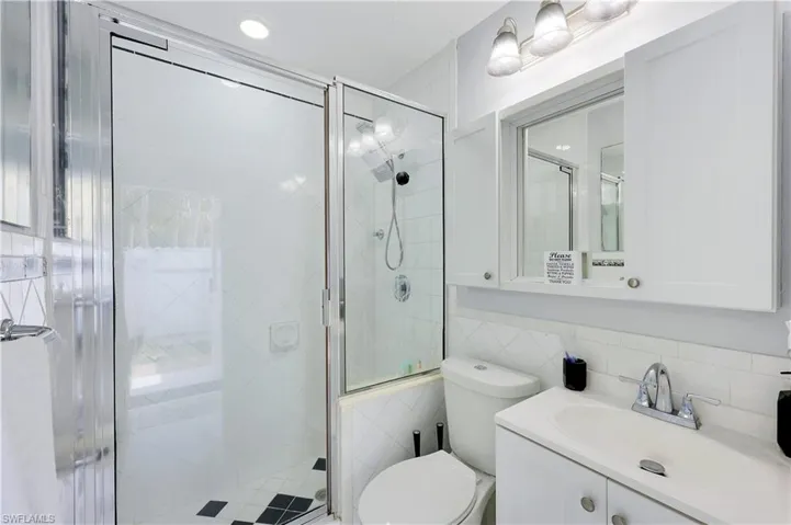 Bathroom with a stall shower, vanity, tile walls, and recessed lighting