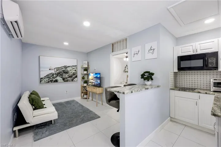 Kitchen featuring light stone countertops, white cabinets, black microwave, backsplash, and recessed lighting