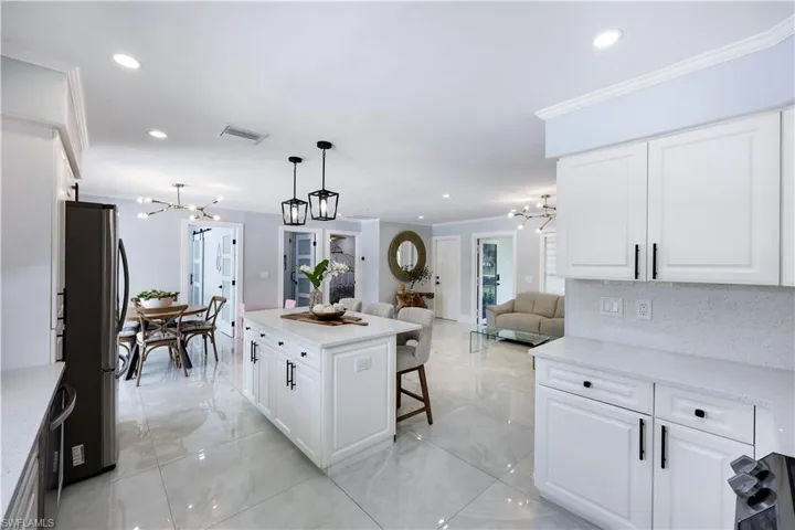 Kitchen featuring suspended lighting, white cabinetry, open floor plan, light stone counters, and crown molding