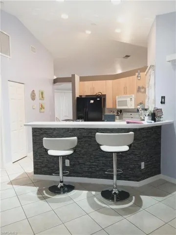Kitchen featuring freestanding refrigerator, white microwave, light brown cabinets, a breakfast bar area, and vaulted ceiling
