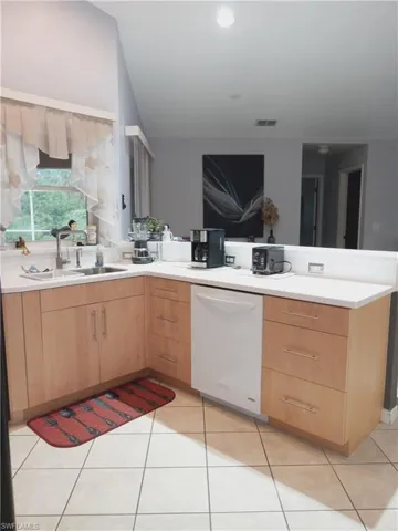 Kitchen with dishwasher, a sink, light brown cabinets, a peninsula, and light countertops