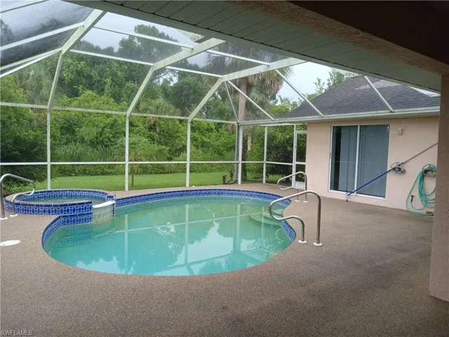 View of swimming pool with a patio area, a pool with connected hot tub, and glass enclosure