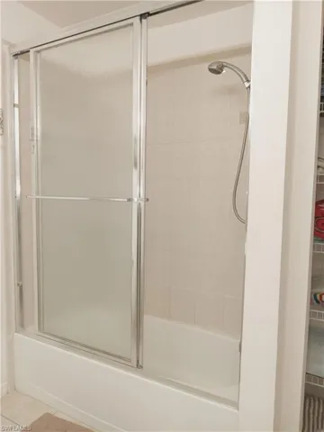 Bathroom featuring combined bath / shower with glass door and tile patterned flooring