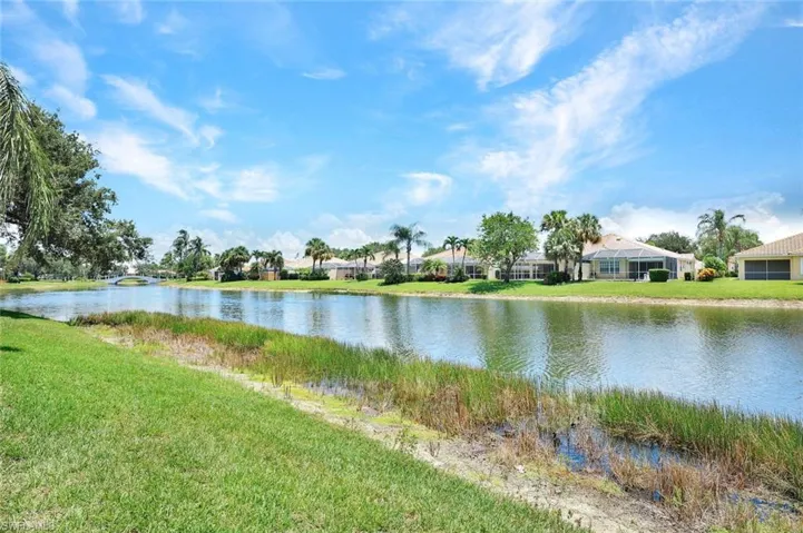 Expansive waterfront property featuring a tranquil canal, lush green lawn, mature trees, and a distant bridge