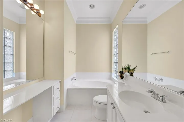 Hers Bathroom featuring a built-in soaking tub, glass block window, double vanity