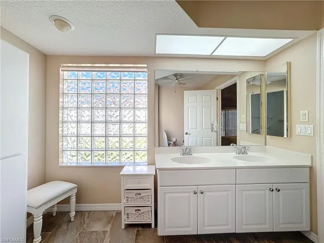 Bathroom featuring double sink vanity, ceiling fan, a textured ceiling, and a skylight