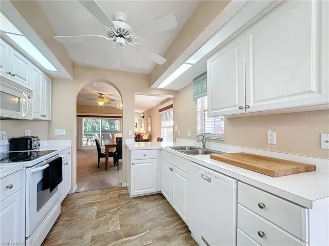 Kitchen featuring light tile flooring, ceiling fan, white cabinetry, sink, and white appliances