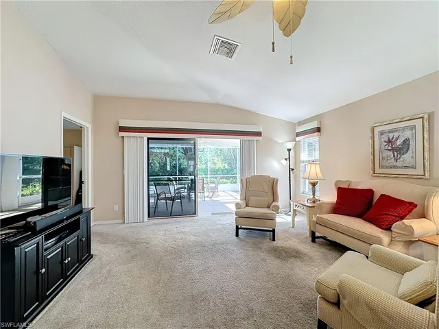 Living room featuring ceiling fan, light carpet, and lofted ceiling