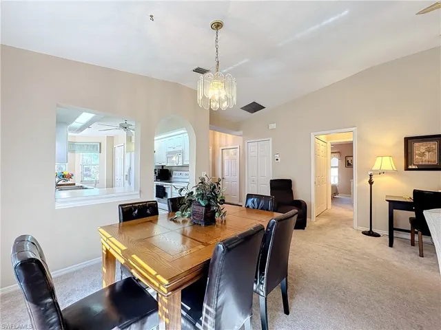 Carpeted dining space featuring vaulted ceiling, sink, and ceiling fan with notable chandelier