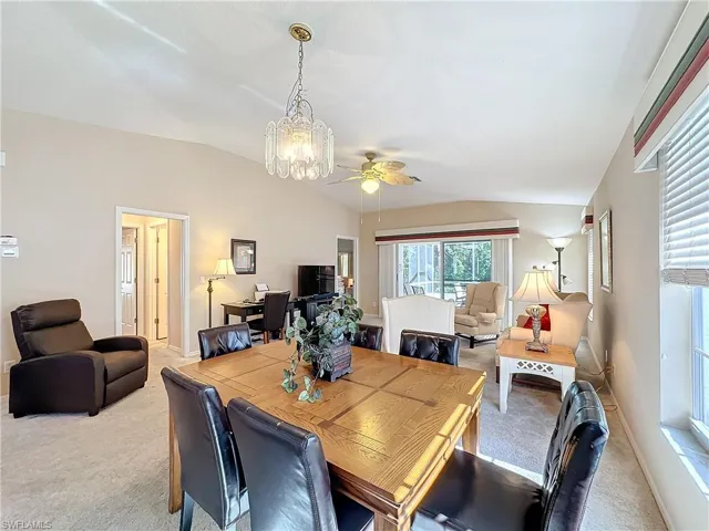 Carpeted dining area with ceiling fan with notable chandelier and lofted ceiling