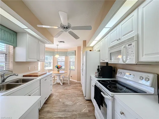 Kitchen featuring white appliances, decorative light fixtures, light tile floors, sink, and white cabinetry