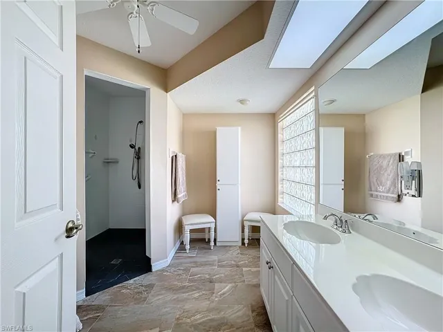 Bathroom with a skylight, ceiling fan, tile floors, a tile shower, and vanity