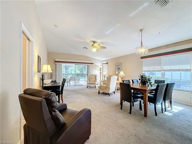 Living room with light carpet, ceiling fan with notable chandelier, and lofted ceiling